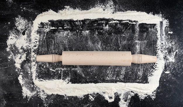 Wooden rolling pin on a black background, top view