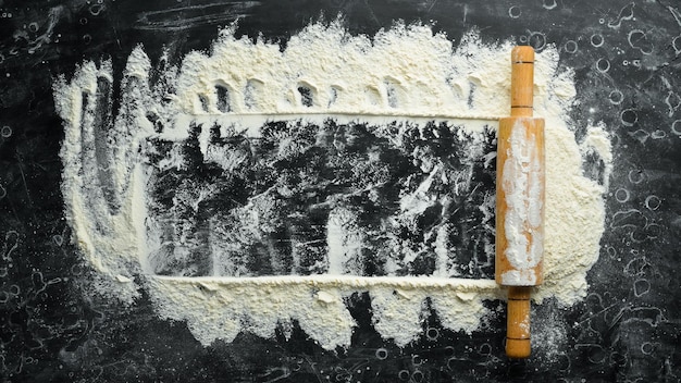 Wooden rolling pin and flour Bakery on a black stone background Top view Free space for text