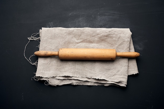 Wooden rolling pin lie on a gray linen napkin, black table