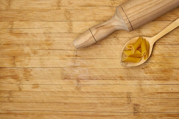 Wooden rolling pin and a wooden spoon filled with penne on a wooden cutting board. Pasta banner.