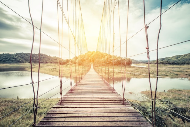 wooden rope Bridge across lake in forest. vintage filter