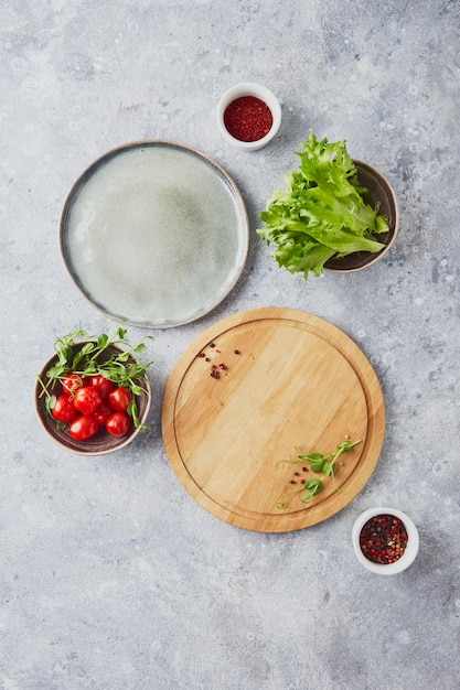 Wooden round cutting board greens vegetables and seasonings on light background