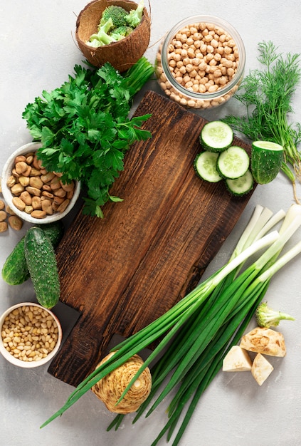 Wooden rustic cutting board with ingredients for cooking vegan food on light background top view