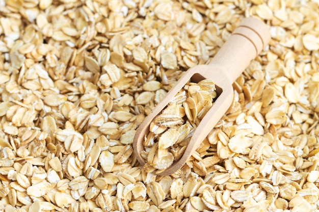 Wooden scoop of dry raw rolled oat flakes top view