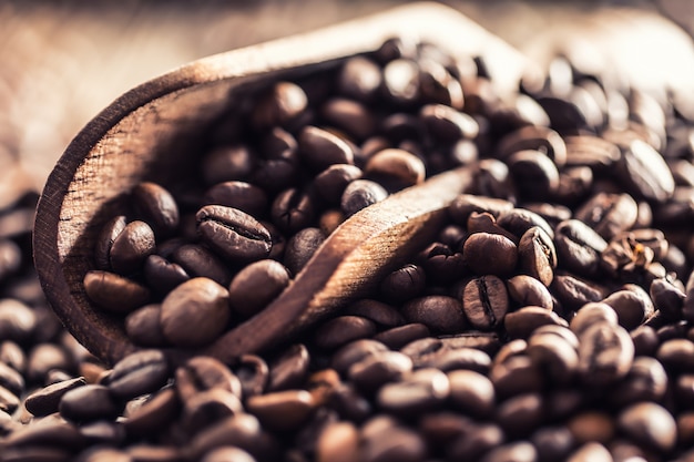 Photo wooden scoop full of coffee beans on old oak table.