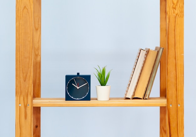 Wooden shelf with alarm clock and objects against blue background