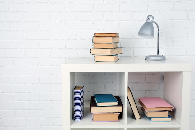 Photo wooden shelf with books and lamp on brick wall background