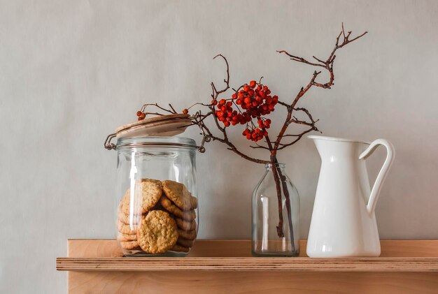 Una mensola in legno con un barattolo di biscotti, una brocca e rami autunnali è una composizione sulla parete della cucina concetto di casa accogliente