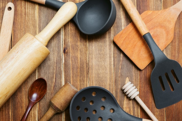 Foto stoviglie in legno e silicone sul tagliere. mestolo, cucchiaio, spatola, mattarello, schiacciapatate e cucchiaio di legno con copia spazio. strumenti di cottura.