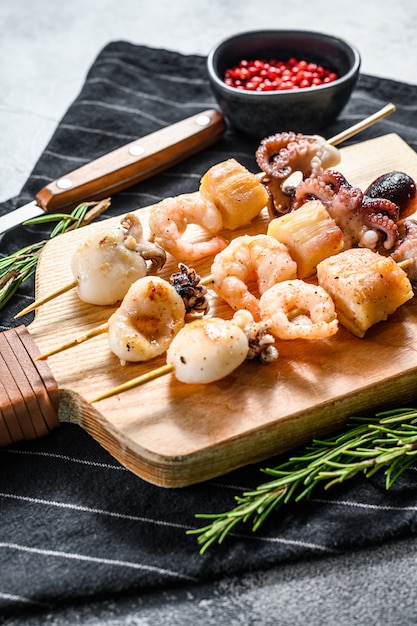 Wooden skewers with grilled seafood, shrimp, octopus, squid and mussels. Gray background. Top view