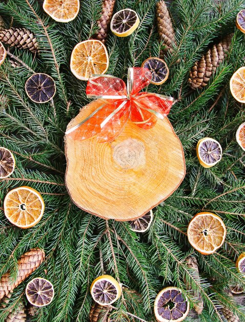 Wooden slice on green fir-tree branches decorated with dried orange slices and cones. Christmas and New Year vintage winter holiday festive composition.