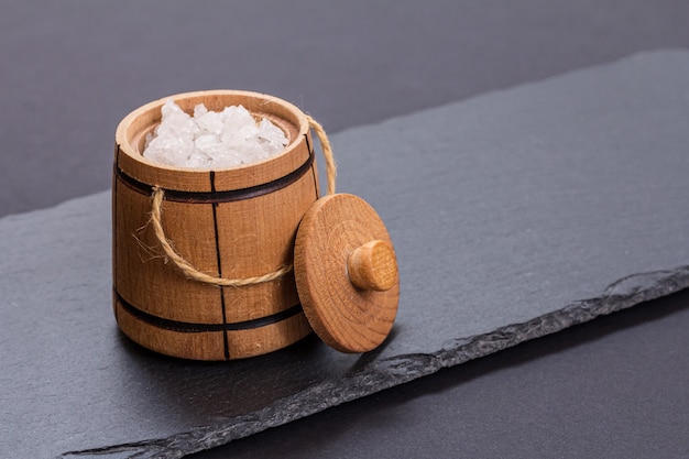 Wooden small barrel for storing salt and a cutting stone board in the black background. Top view.