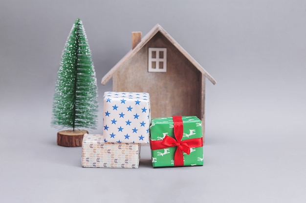Деревянный домик с подарками и рождественской елкой на сером фоне. Новогодняя композиция. Рождественские подарки.