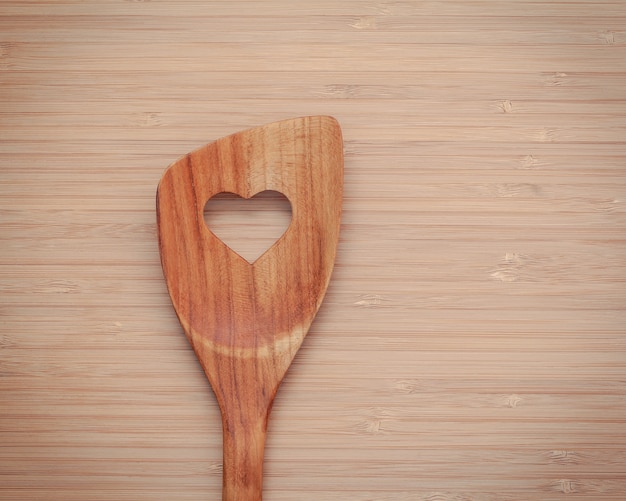 Wooden spatula with heart shape hole on bamboo cutting board with flat lay and copy space.