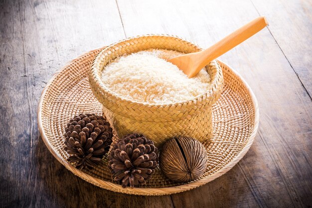 wooden spoon in basket of jasmine rice and pine cones on wooden table