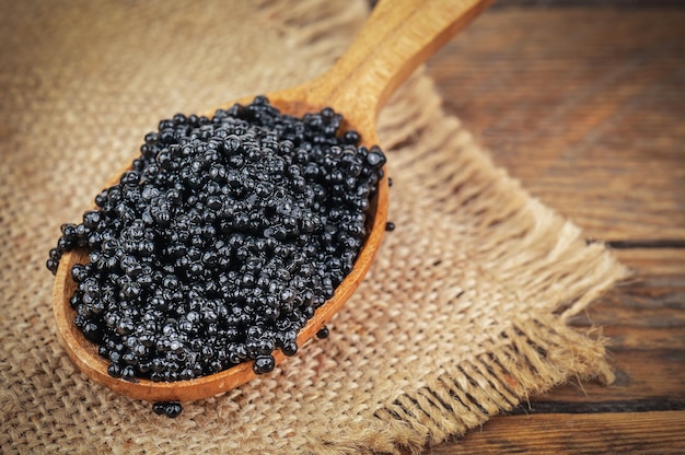 Wooden spoon of black caviar on burlap napkin