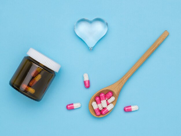 A wooden spoon and a bottle of medicinal capsules and a glass heart