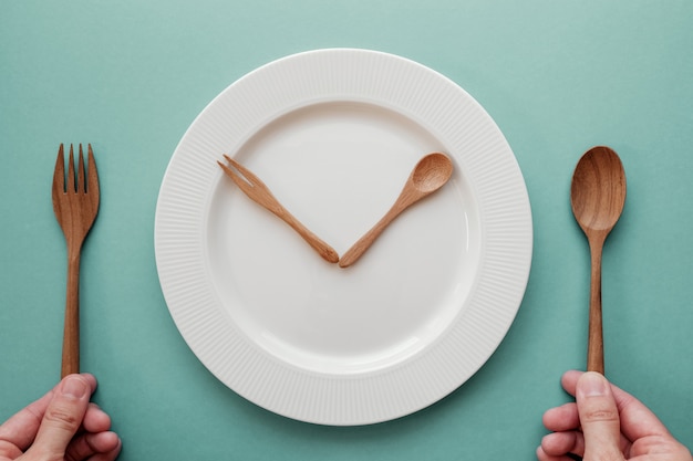 Foto cucchiaio e forchetta di legno come lancette di un orologio sul piatto bianco