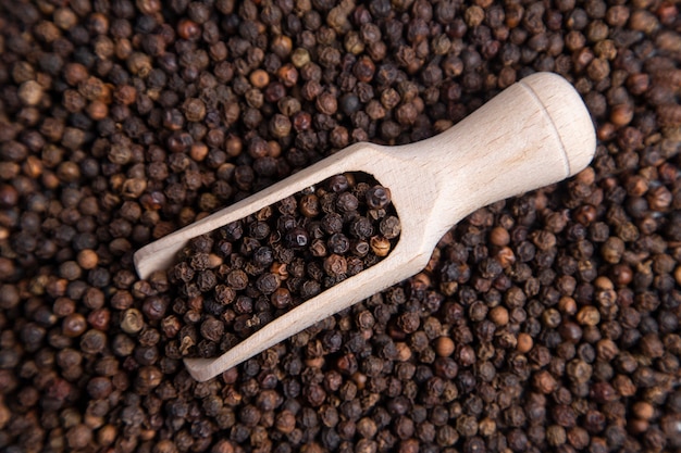 A wooden spoon full of black pepper corns .