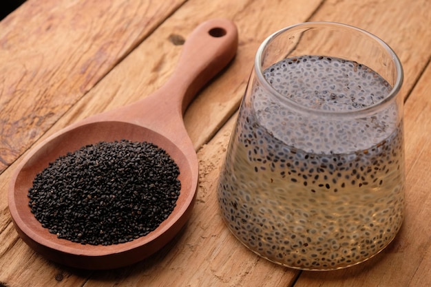 A wooden spoon and a glass of liquid sit on a wooden table basil seeds selasih