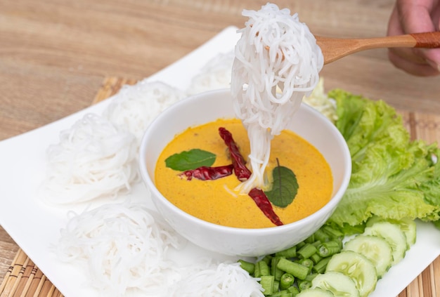 A wooden spoon picking up rice noodles on a white plate on a\
food and drink background