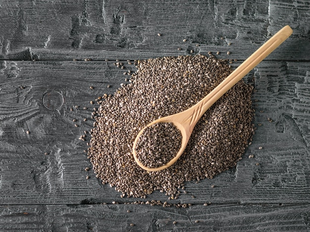 Photo wooden spoon on a pile of black chia seeds. the view from the top. flat lay.