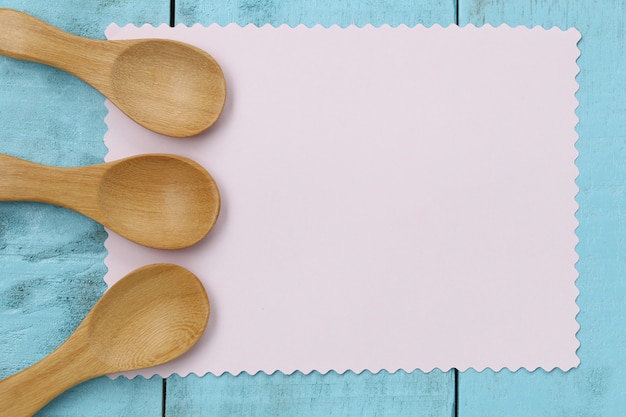 Деревянная ложка на розовой бумаге для заметок и синий деревянный стол.