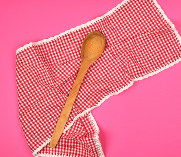 Wooden spoon on a red kitchen towel, pink background