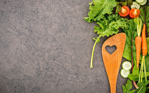 Wooden spoon and vegetables on dark stone background.