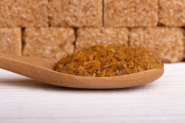 Wooden spoon with cane sugar against the background of a wall of sugar cubes