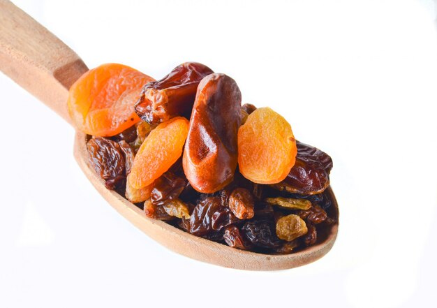 Wooden spoon with dates, dried apricots, raisins isolated on white.