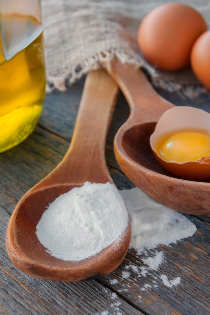 Wooden spoon with flour, eggs and a bottle of oil