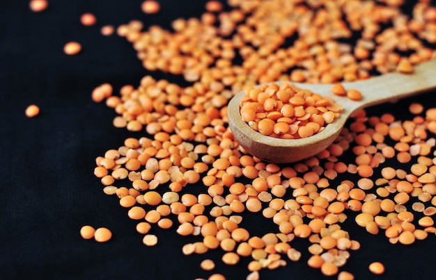 A wooden spoon with lentils on a dark surface surrounded by lots of lentils