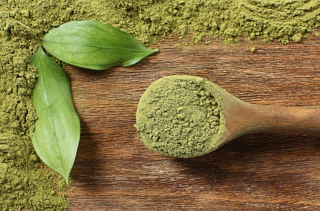 Wooden spoon with powdered matcha green tea on wooden table