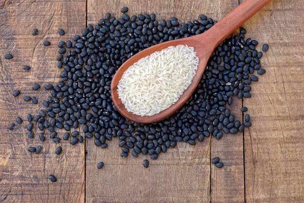 Wooden spoon with raw rice over heap of beans