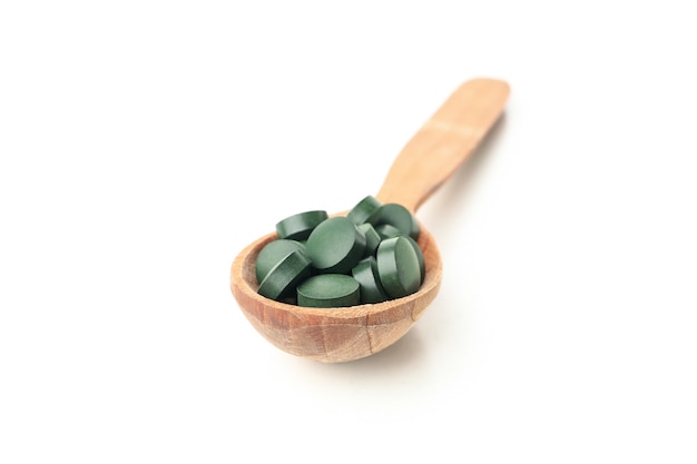 Wooden spoon with spirulina pills isolated on white background