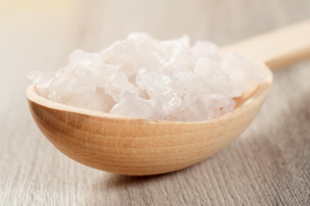 Wooden spoon with white sea salt for bathroom procedures. Spa products and accessories. Close up with selective focus on salt