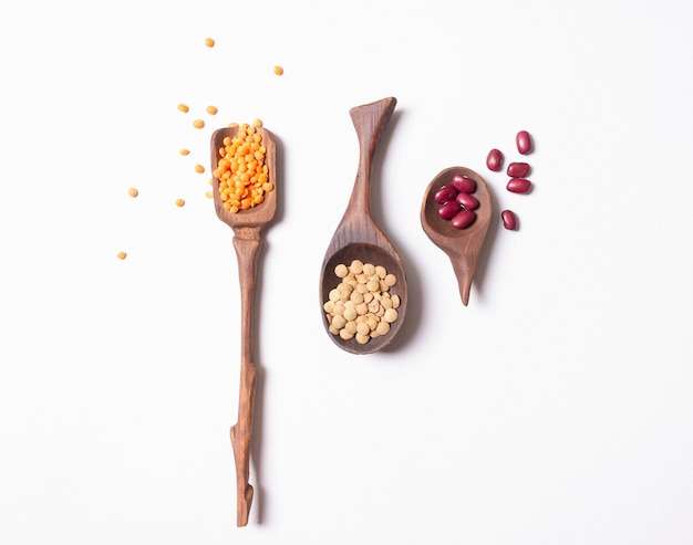 Wooden spoons with beans lentils on white background