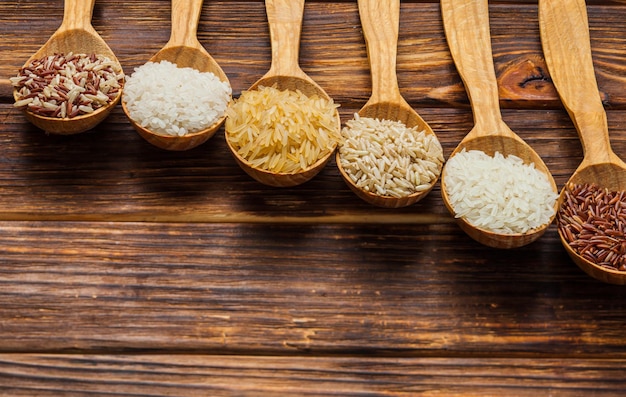 Wooden spoons with different rice types on the wooden background