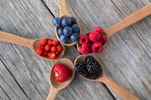 Wooden spoons with forest berries on an old wooden board