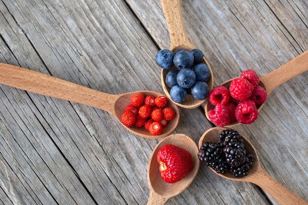 Wooden spoons with forest berries on an old wooden board