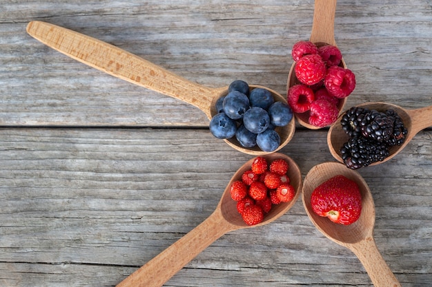 Wooden spoons with forest berries on an old wooden board