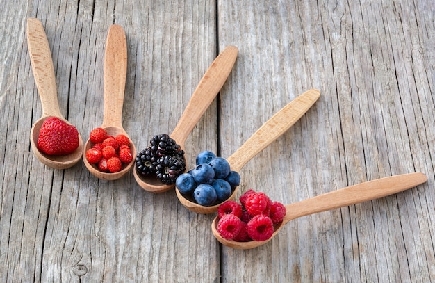 Wooden spoons with forest berries on an old wooden board