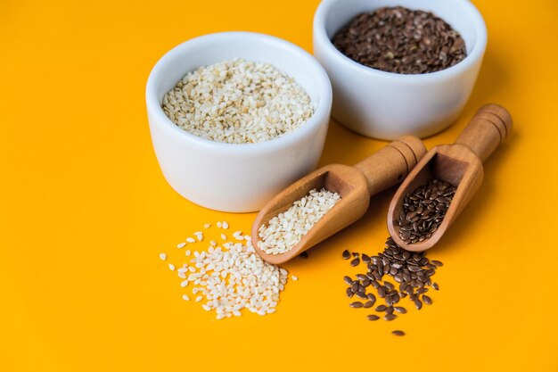 Wooden spoons with sesame and flax seeds lies in a white mortar on a yellow background healthy eat