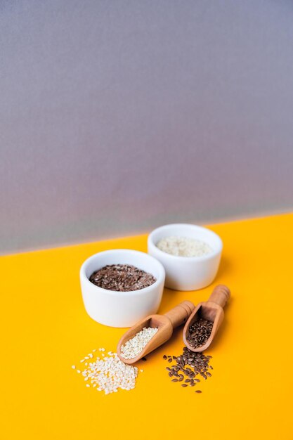 Wooden spoons with sesame and flax seeds lies in a white mortar on a yellow background healthy