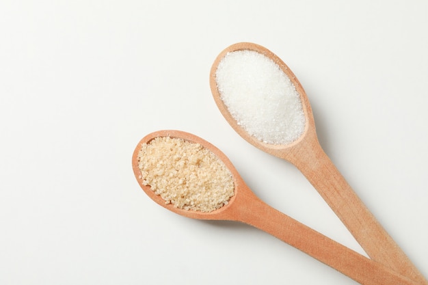 Wooden spoons with sugar on white background, top view