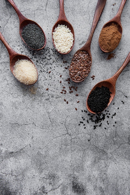 Wooden spoons with various healthy seeds and spices on gray concrete desk
