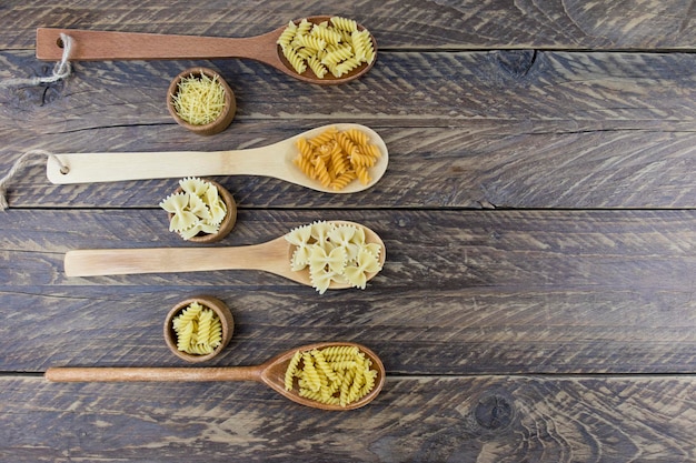 Wooden spoons and wooden bowls with dry Italian pasta of different shapes on a rustic brown table. top view.