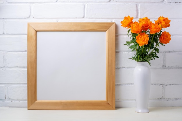 Wooden square picture frame mockup with globeflowers near white painted brick wall Empty frame mock up for presentation design Template framing for modern art