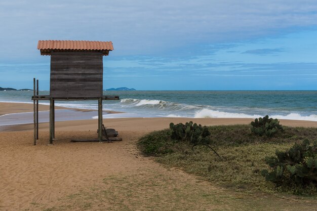 Wooden structure in the shape of a lifeguard house on the beach of Rio das Ostras in Rio de Janeiro. Partly cloudy day, blue sky and some clouds. Strong sea and yellowish sand and lots of rocks.